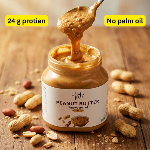 Jar of peanut butter with a spoonful being lifted, surrounded by peanuts on a wooden surface.