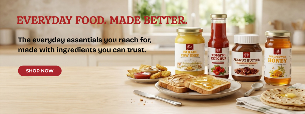 A breakfast spread of peanut butter, tomato ketchup, honey, and banana spread arranged on a wooden table with toast, fruit, and a spoon. Large text at the top reads 'EVERYDAY FOOD.